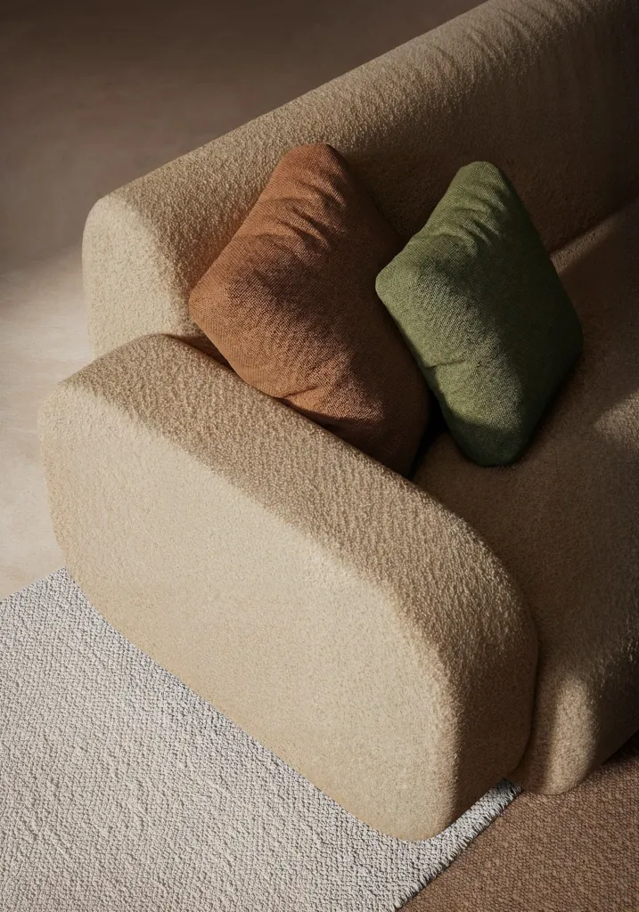 Dettaglio del bracciolo arrotondato del divano con cuscini terracotta e verde salvia