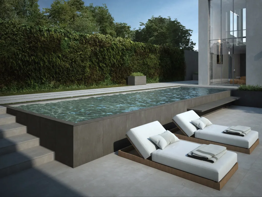 Piscina con bordo in gres Porcelaingres e due lettini bianchi in un giardino con parete verde